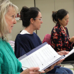 Three female singers rehearse.